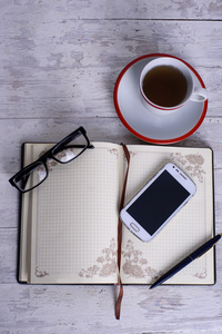 杯 记事本 手机 眼镜和笔在白色的老式木制背景上