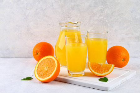 玻璃杯和一壶新鲜橙汁, 带橙色和黄色的切片, 在浅灰色的桌子上