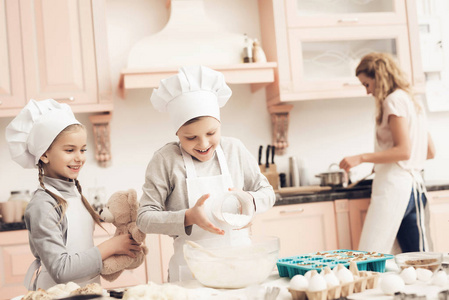 母亲教她的孩子用白帽子在厨房准备饼干