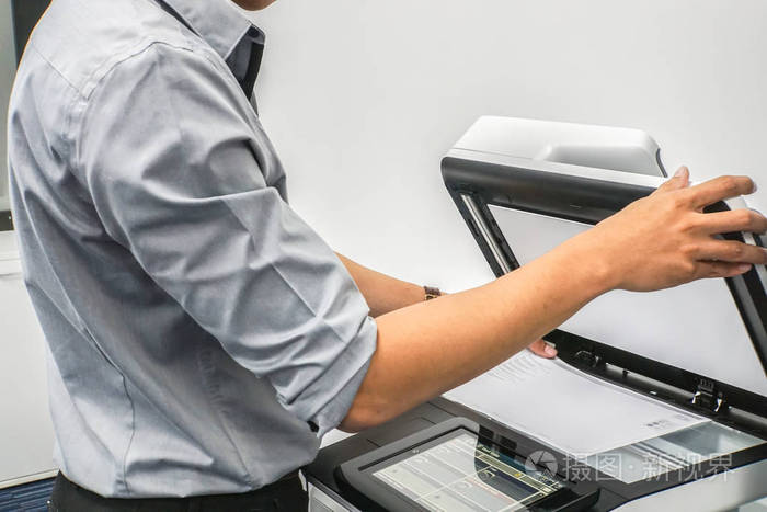 穿灰色衬衣的商人用打印机扫描办公室里的重要和机密文件照片-正版