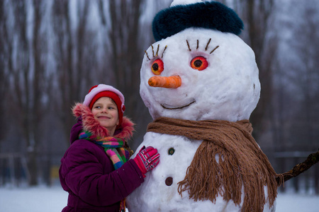 一个快乐的小女孩在大滑稽的雪人附近。一个可爱的小女孩在冬季公园里玩得很开心, 冬天