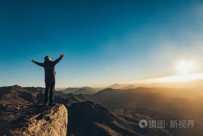 人站立面对上升的太阳与举起他的胳膊在西奈登上