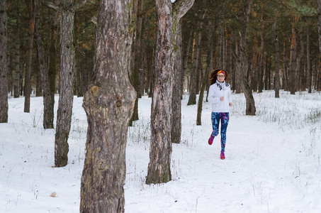 运动年轻女人在冬季森林中运行