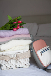 床上有干净东西的篮子。舒适.针织毛衣, 背包, 郁金香花束。春季服装