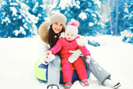 幸福的母亲和孩子一起坐在雪橇在冬季雪上
