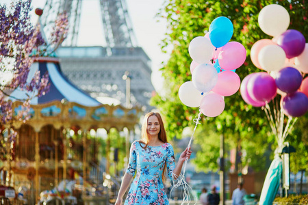 快乐的年轻女孩的粉色和蓝色气球在埃菲尔铁塔和巴黎，法国的旋转木马前一堆