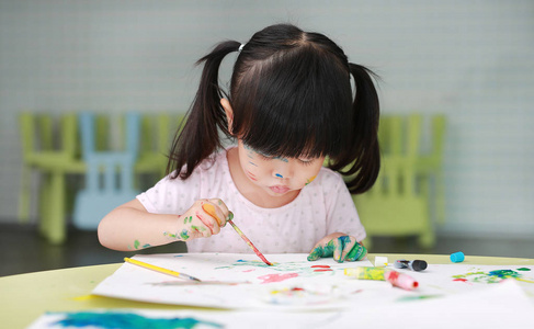 儿童女孩用画笔和水的颜色绘画。孩子活动概念