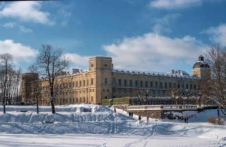 从 Karpin 池塘边的 Gatchina 宫的景色。冬天, 雪覆盖着山坡。宫殿的雄伟城墙被太阳照亮。Gatchina, 俄罗