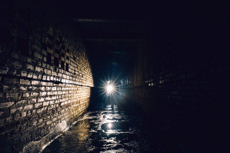 在黑暗肮脏的砖地下隧道或下水道走廊的人用手电筒