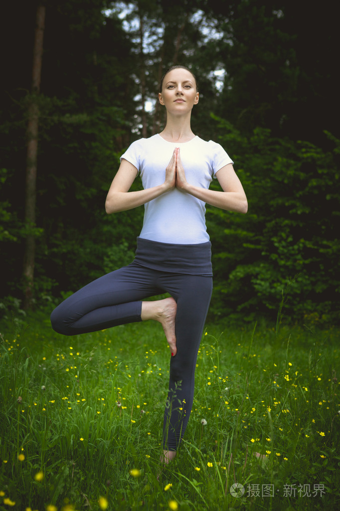 幸福的年轻女人站在瑜伽姿势 vrikshasana 在草地上