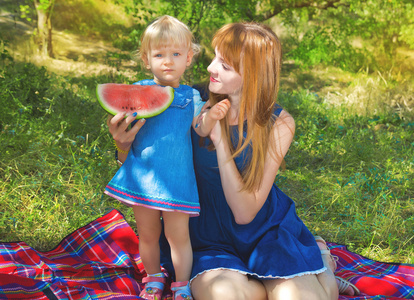 年轻的母亲和孩子坐在公园里，吃西瓜