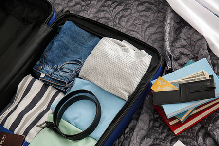 钱包, 成堆的书和打开的手提箱与包装的东西在床上