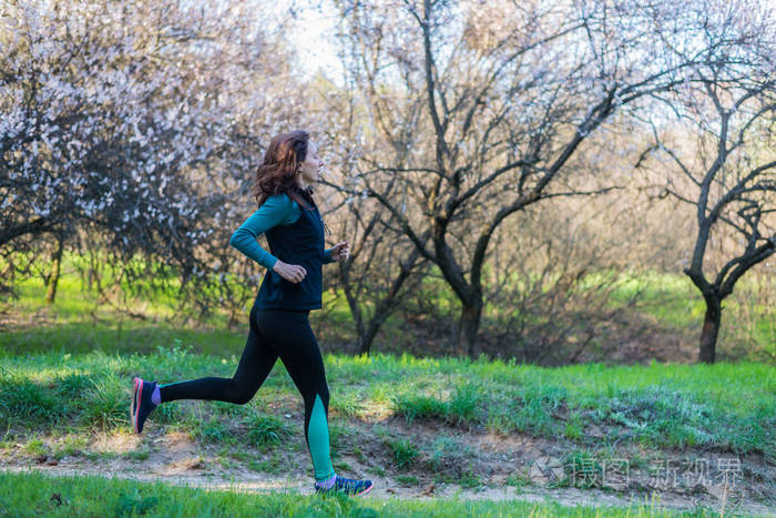 年轻妇女在早晨奔跑通过春天森林
