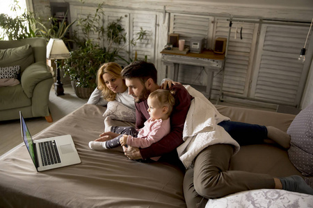 幸福的家庭躺在床上, 在卧室里看着笔记本电脑上的东西