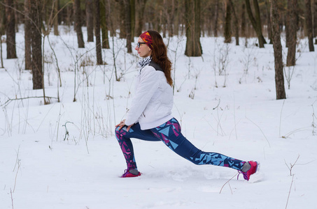 运动年轻女人做健身冬季的森林里