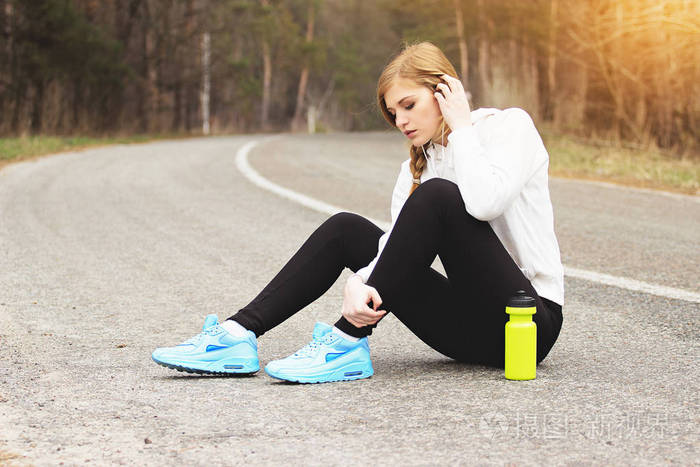运动损伤美丽和年轻的红发女孩抱着她受伤的腿坐在公园路