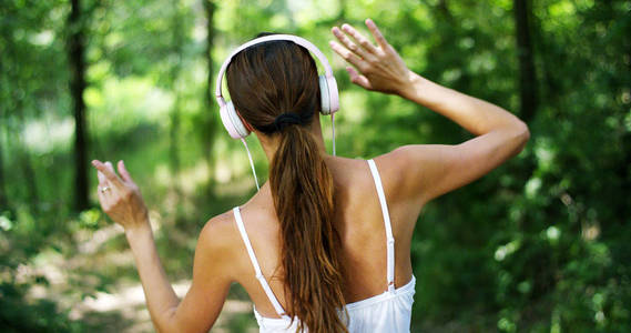 一个女人在绿色戴着耳机听音乐，唱歌，跳舞，玩无忧无虑的空气。音乐给了他的能量来唱，幸福美满。音乐使放飞想象