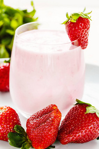 大型成熟草莓和一杯饮用酸奶在明亮的背景上