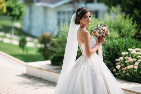 美丽的新娘化妆和婚后发型结婚。时装模特的肖像在华丽的白色婚纱礼服与花束的花朵在她的手中。家庭概念