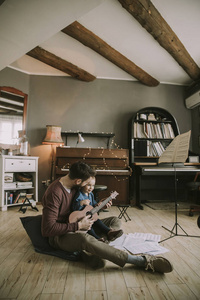 年轻的父亲和小女儿在家里玩声学吉他在房间里