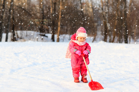 可爱的小姑娘蹒跚学步挖在冬天的雪