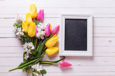 一束明亮的春天郁金香和苹果树的花朵, 空白的黑板上白色的木质背景。选择性对焦。文本的位置。顶部视图