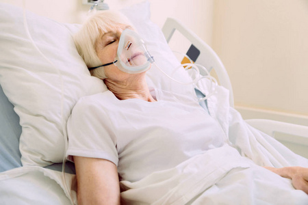 戴氧气面罩的老年妇女躺在病床上