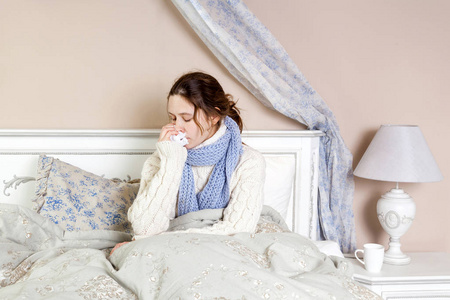 流感。特写镜头的郁闷生病的女人躺在床上厚厚的蓝色围巾，握住她的鼻子组织