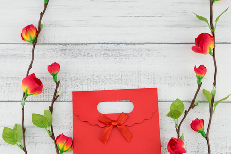 红色礼物袋子与假红色花分支在白色木头背景与拷贝空间