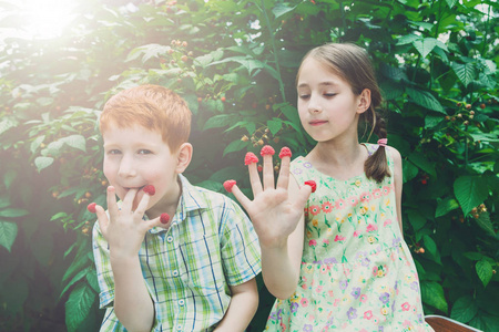 快乐的孩子们在夏天花园里吃覆盆子从手指