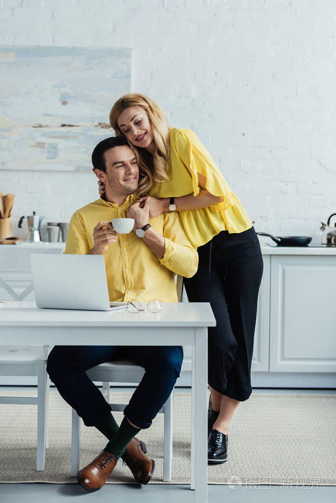 金发女郎拥抱咖啡机工作的人用笔记本电脑