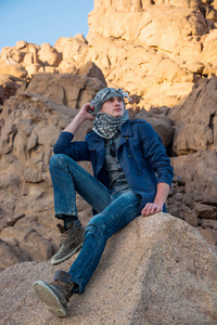 头巾，坐在一块岩石在沙漠中的人