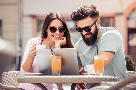 快乐情侣坐在咖啡馆里喝咖啡, 看笔记本电脑, 微笑着喝果汁