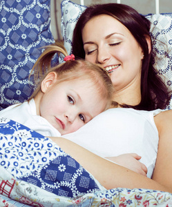 母亲和女儿的肖像躺在床上, 微笑着接近