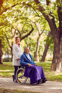 老人坐在轮椅与在公园里的护士
