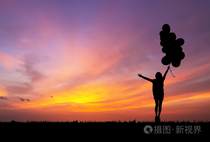拿着空气气球跑束在日落时的剪影的女孩
