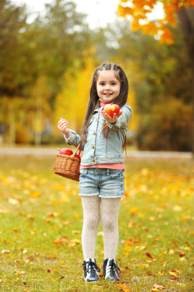 漂亮的小女孩抱着篮子里的苹果,户外