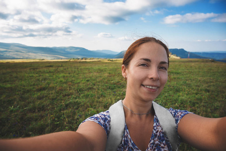 微笑的年轻妇女采取自拍在山背景, 夏天旅行