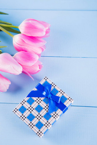 束粉红色郁金香与礼品盒上蓝色的木制背景