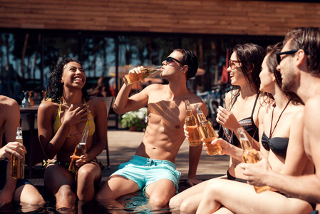 夏季, 年轻的朋友们在游泳池里用啤酒瓶欢呼。游泳池派对在游泳池的朋友的族裔公司