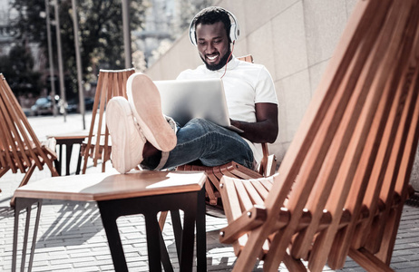 快乐的非洲裔美国绅士听音乐, 而使用笔记本电脑