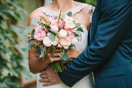 美丽的新娘在一条白色的连衣裙，抱着花束从春天的花和她的新郎拥抱她。婚礼花束。爱的时刻