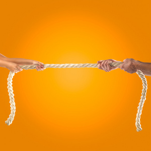 手女孩和成年男子用力拉绳子上橙色背景。竞争理念