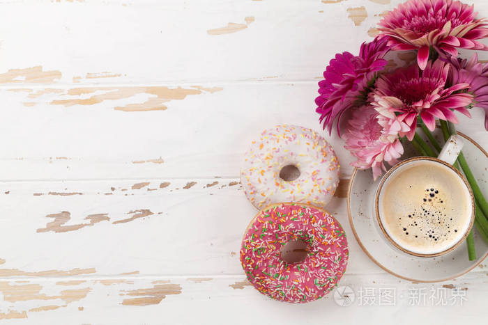 咖啡杯, 甜甜圈和非洲菊花在白色的木桌上。具有文本空间的顶部视图