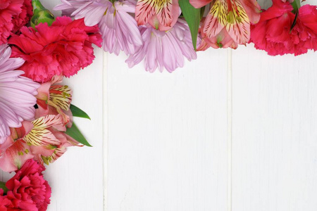 粉红色康乃馨, 菊花和百合花的角落边界反对白色木头背景