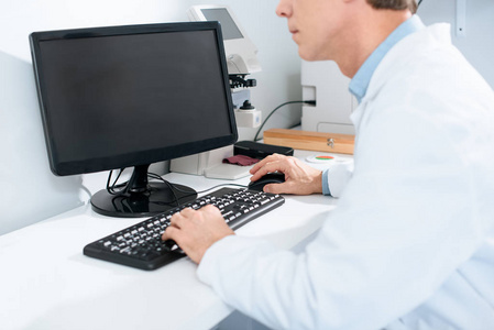 男性眼镜师在临床中使用计算机的裁剪视图