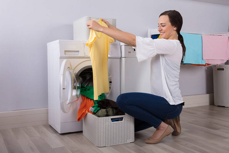 快乐的年轻女人看着清洁的黄色 t恤洗涤后清洗机
