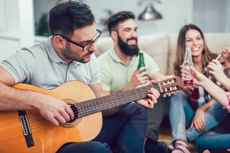 一组快乐的年轻朋友与吉他有乐趣和喝啤酒在家室内