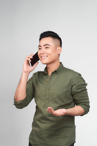 年轻的亚裔男子的肖像在电话站在灰色背景下说话