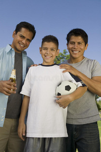 男孩1315岁拿着足球站在室外，两兄弟正对着。